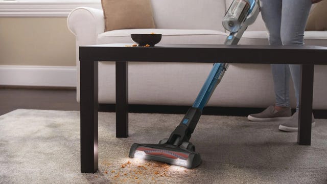 Black and Decker PowerSeries Extreme Stick Vac with LED headlights cleaning a mess on the carpet under a table