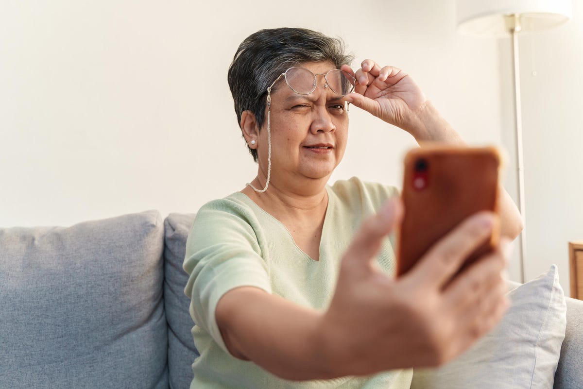 Woman holding glasses up and squinting at phone