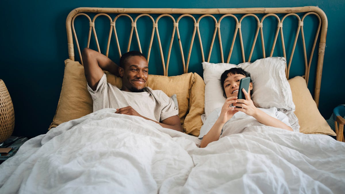 Woman showing a man something on her phone while they lay in bed