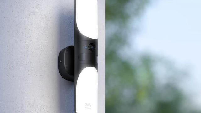 The Eufy wired wall light cam attached to a gray outdoor wall with lights on.