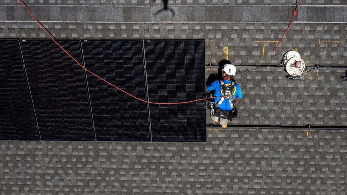 A solar installer wires up solar panels on a gray rooftop.