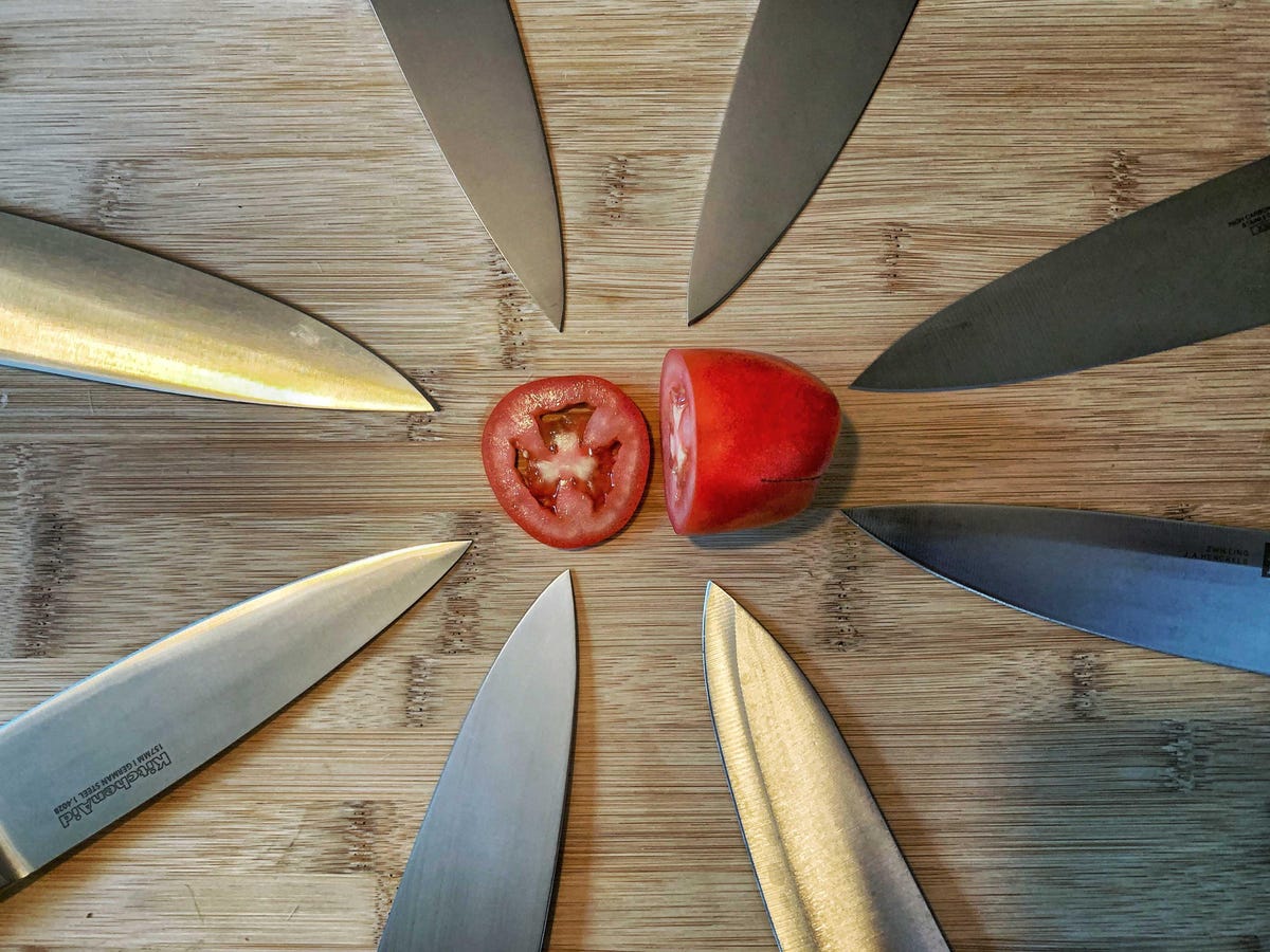 a circle of chef's knives surrounding a sliced tomato