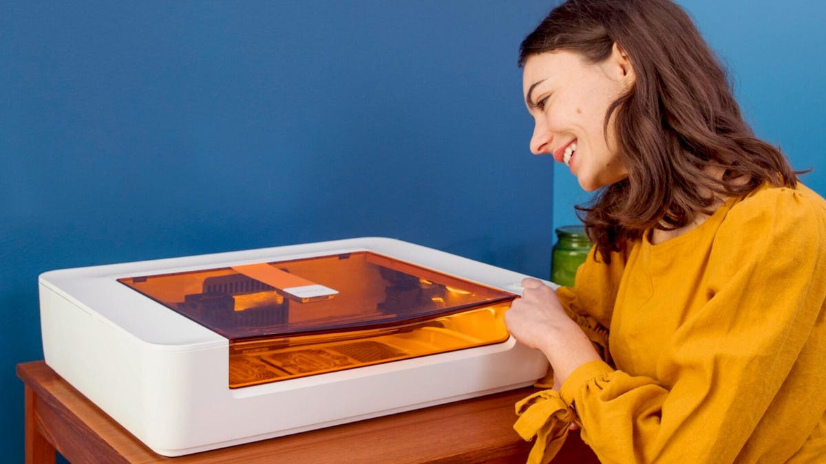A white laser cutter with orange cover and a lady laughing