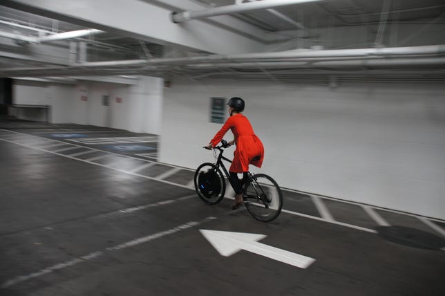 A rider in a red dress bikes away in a white parking garage.