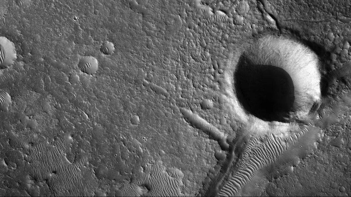 A black-and-white view of ridged Martian landscape with a dark crater in the corner.