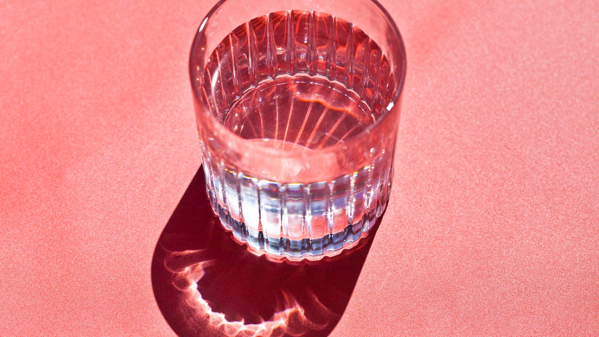 A glass of water against a coral background