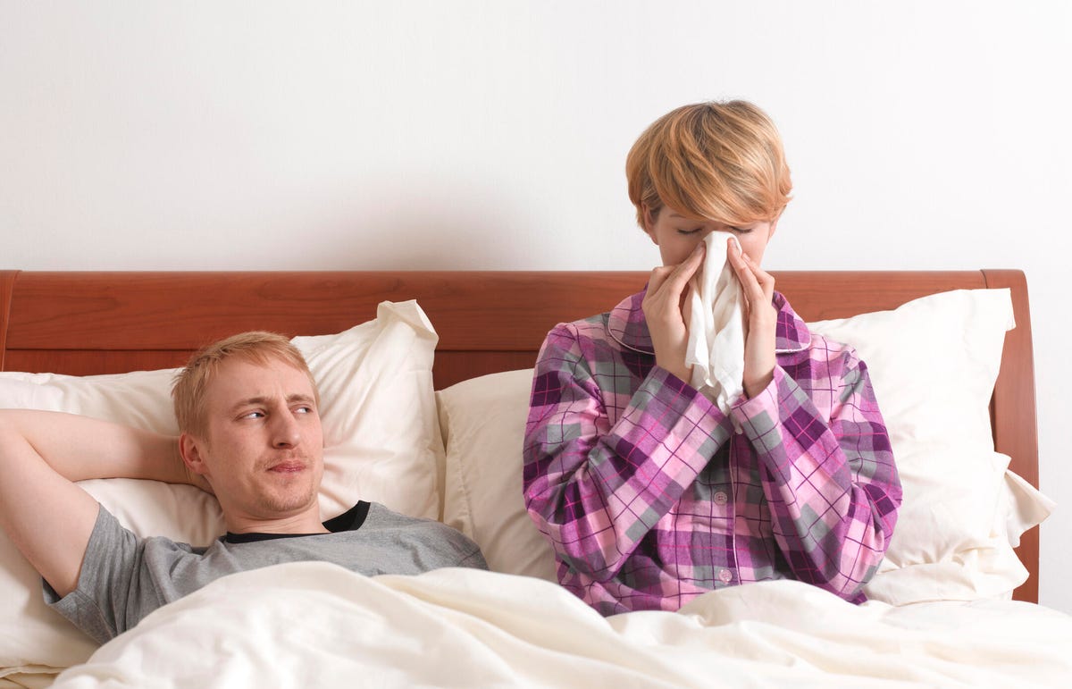 Couple sitting in bed while woman blows her nose.