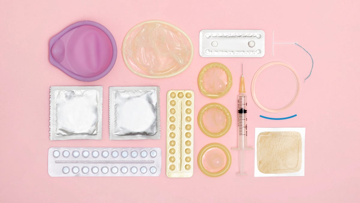 Condoms, the pill and other birth control methods lined up on a pink background.
