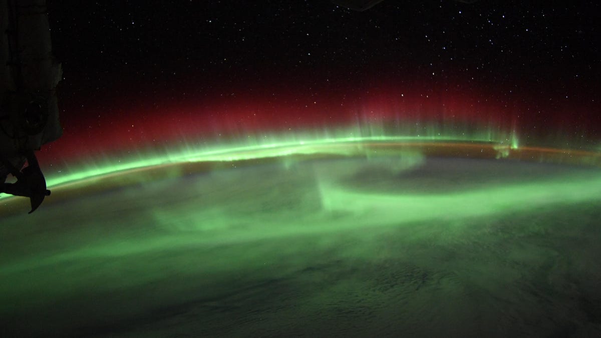 Glowing green aurora pops out over the curve of Earth with stars showing through in space in the background.