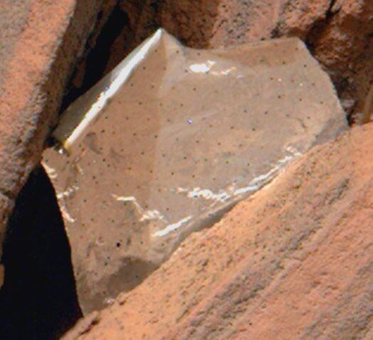 Close-up, cropped view of a light-colored piece of foil with dots across it tucked into a rock on Mars.