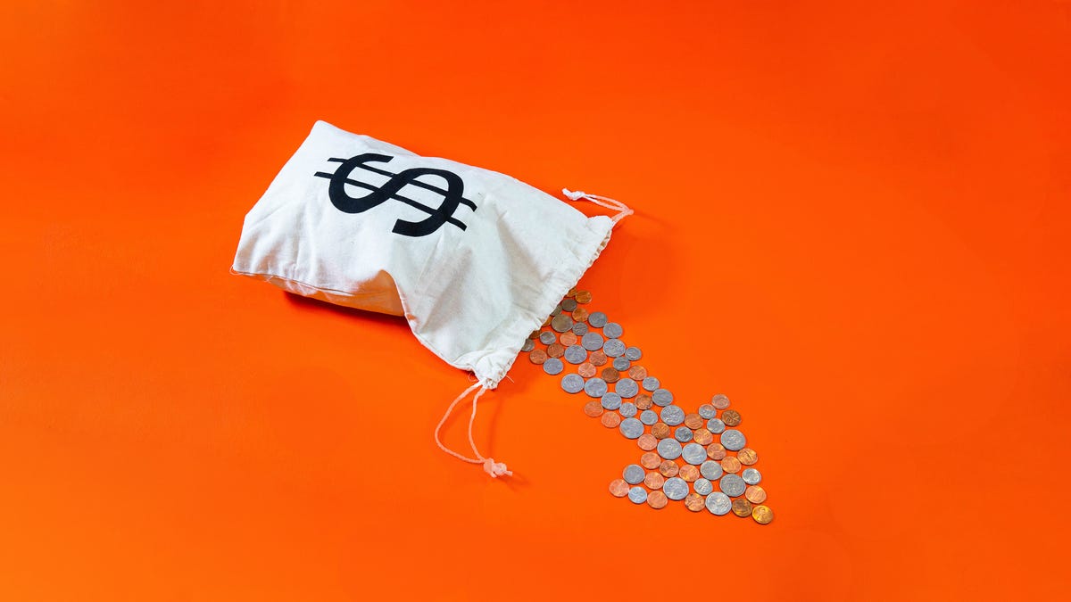 A bag of money tipped over with change pouring out in the shape of a downward arrow