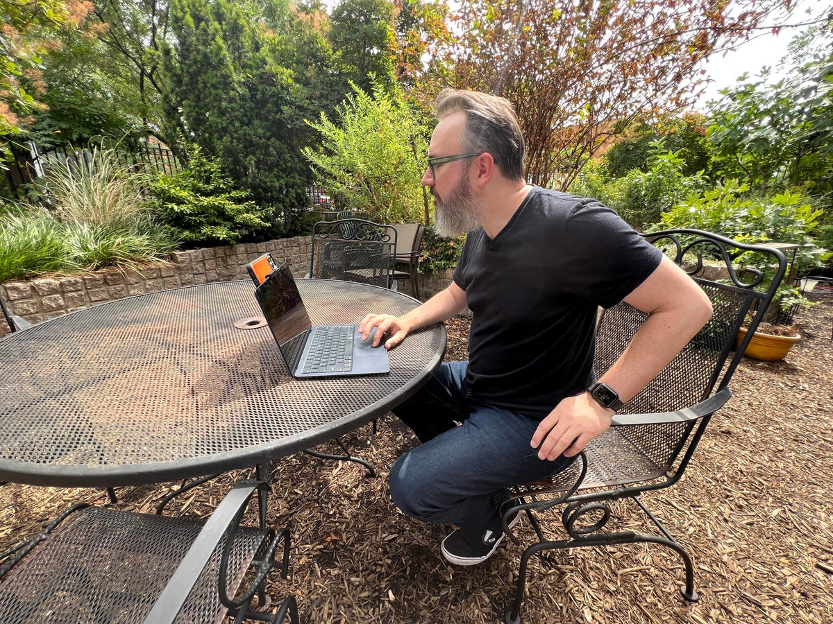 Dan Ackerman sentado en una mesa del patio mirando una computadora portátil