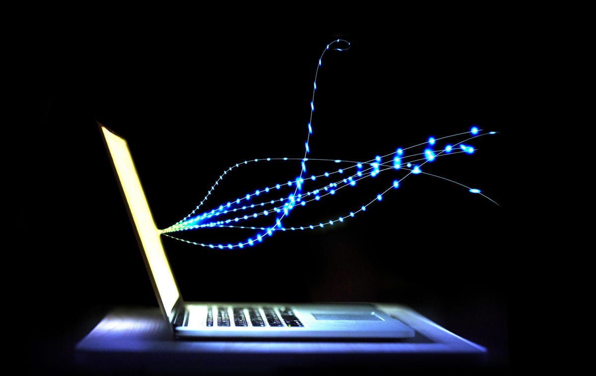 A laptop glows in the dark with stylized signal emerging from the bright display