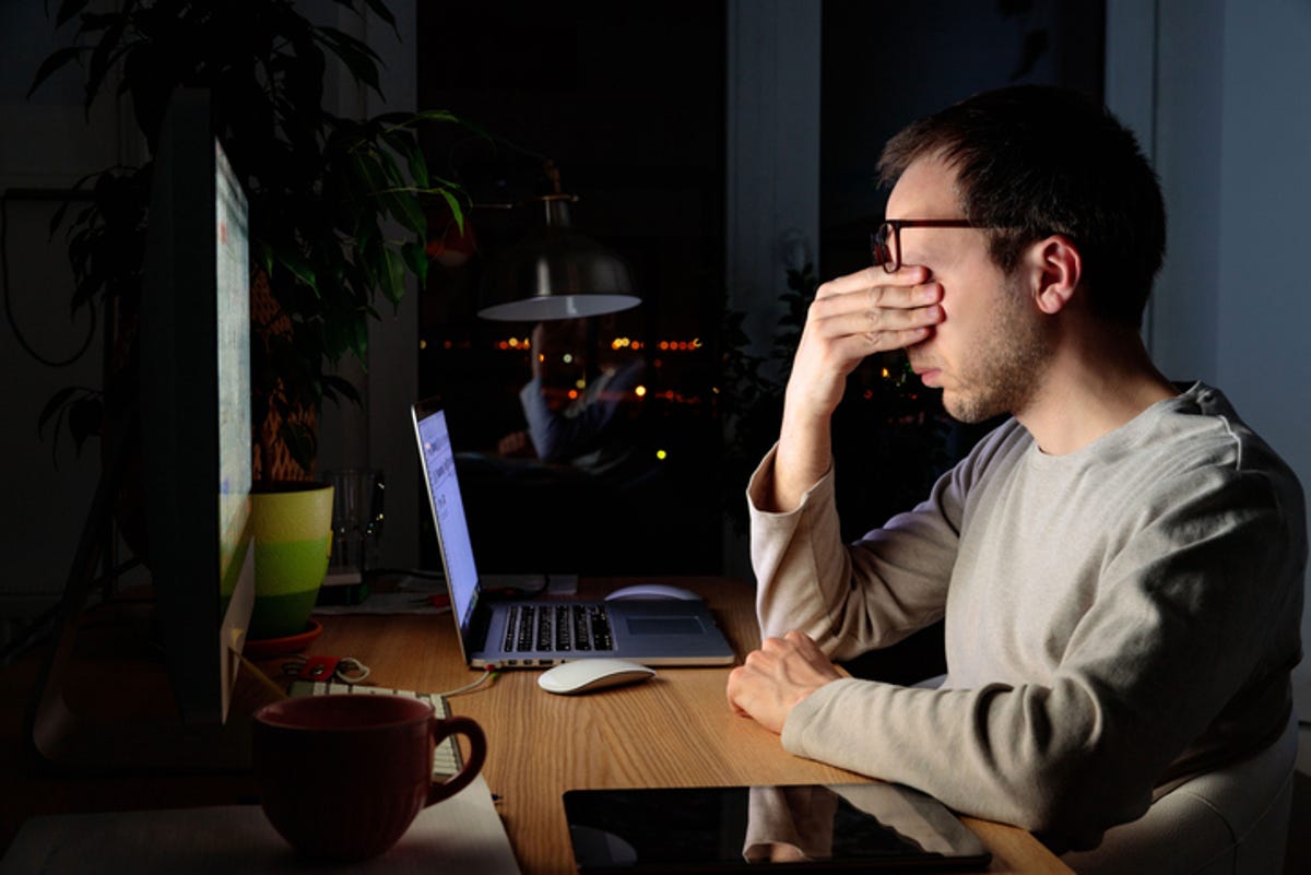 Un hombre se sienta frente a una computadora en la oscuridad y se frota los ojos.