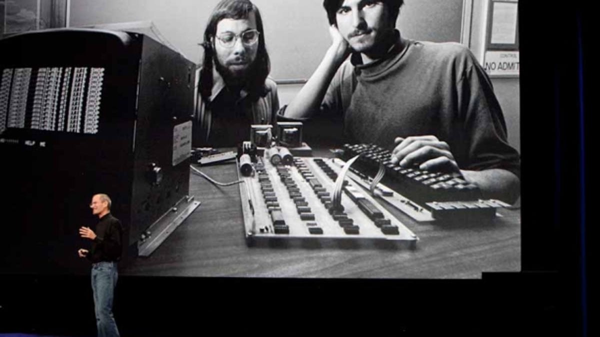 Steve Jobs giving a talk in 2010 in front of a large black-and-white picture of Steve Jobs and Steve Wozniak in 1976