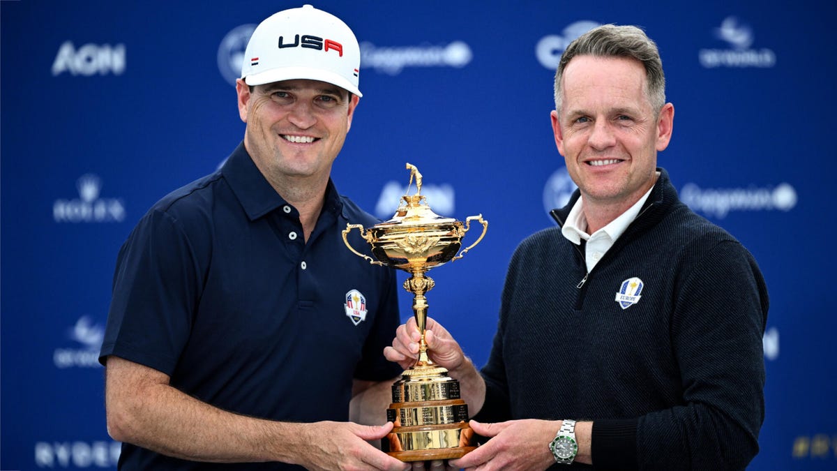 Team captains Zach Johnson and Luke Donald holding the Ryder Cup together in front of a blue background.