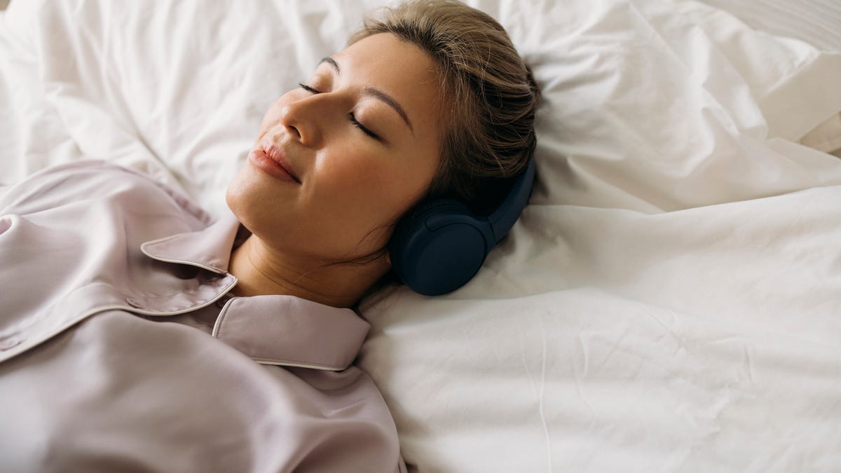 A woman using headphones to listen to sound while lying in bed.