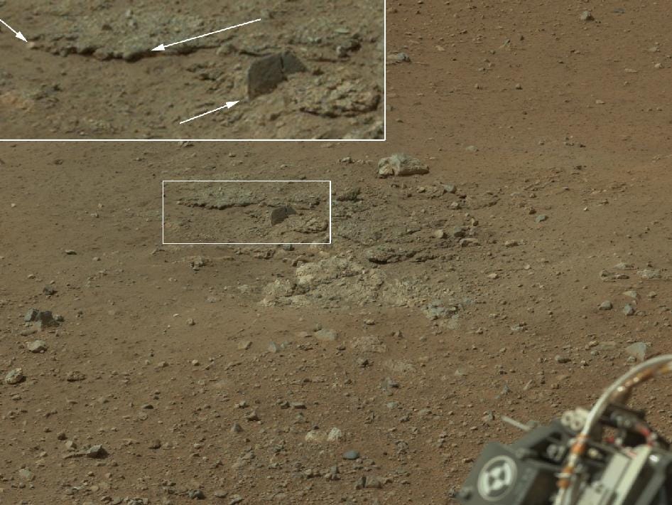 Rockets from the descent stage of the rover's landing last week blew away fine dust on the surface, uncovering the bedrock below. Of particular note, NASA says, is a well-defined, topmost layer that contains fragments of rock embedded in a matrix of finer material, Seen here in the inset of the image are pebbles up to 1.25 inches  across (the upper two arrows) and a larger clast 4 inches long protruding up by about 2 inches from the layer in which it is embedded. Clast-rich sedimentary layers can form in a number of ways. Their mechanisms of formation can be distinguished by the size, shape, surface textures, and positioning with respect to each other of the fragments in the layers.