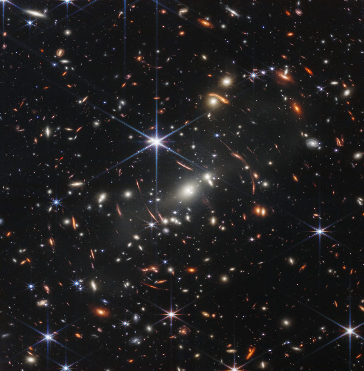 A field of thousands of galaxies against the dark of space with a large central six-pointed blue star.