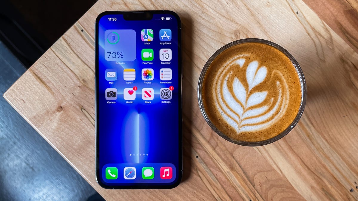 An iPhone 13 Pro Max on a table next to a latte
