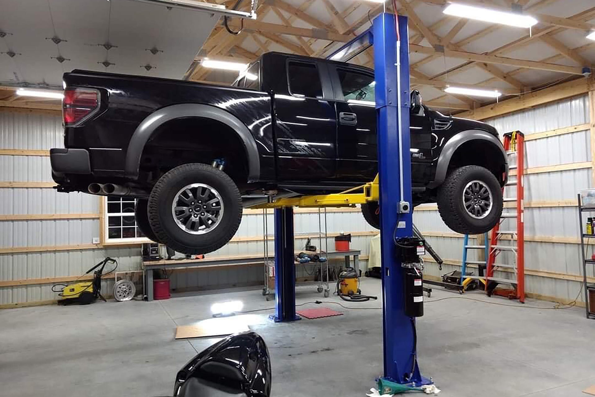A black pickup truck lifted up by a two-post auto lift.