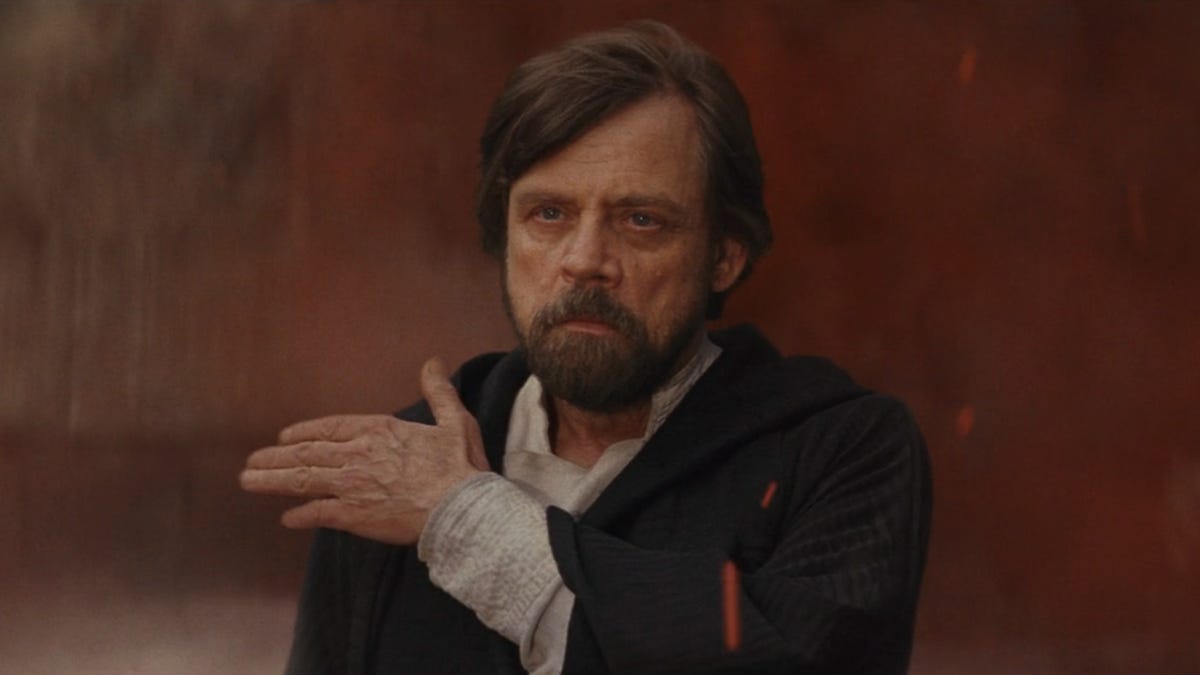 Luke Skywalker brushes off his shoulder as red dust swirls around him in The Last Jedi.