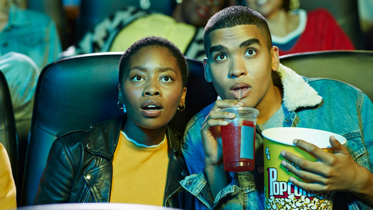 A young couple eats popcorn while watching a movie in a theater