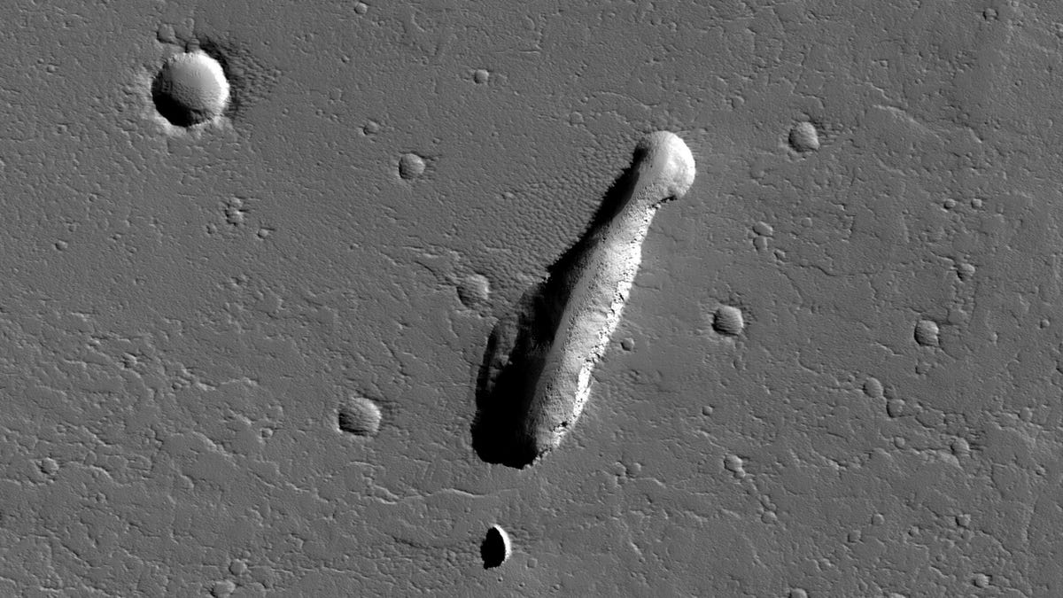Black-and-white overhead view of Mars landscape with a heavily shadowed elongated pit.