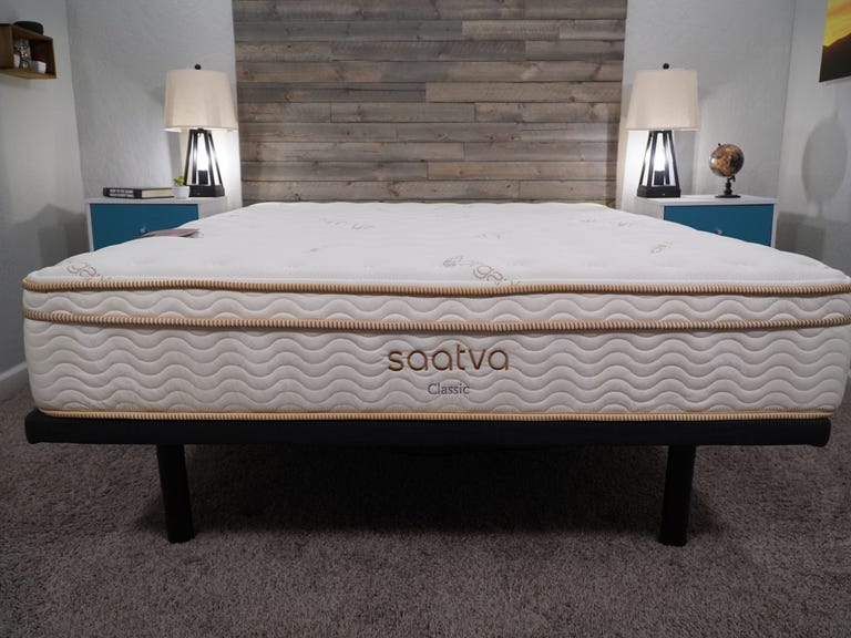 A Saatva Classic mattress on a standard black bed frame against a wooden backdrop