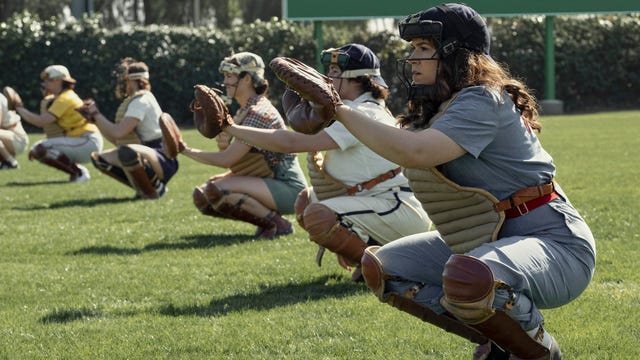 The Rockford Peaches in a line, all squatting and raising their mitts to catch a ball.