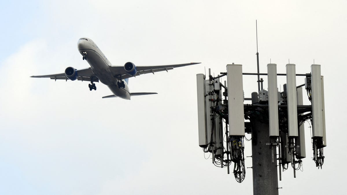 A passenger jet flies over a cell signal tower.