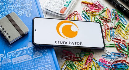 Crunchyroll logo on a smartphone on top of a pile of paperclips and other office supplies
