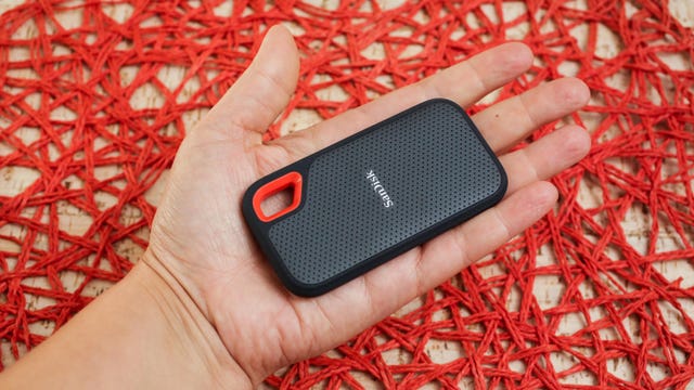 A hand holding a pocket-sized SanDisk Extreme 2TB portable storage drive.