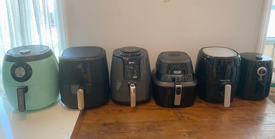 Six different air fryers lined up on a table