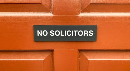 A "no solicitors" sign on a reddish-orange door.