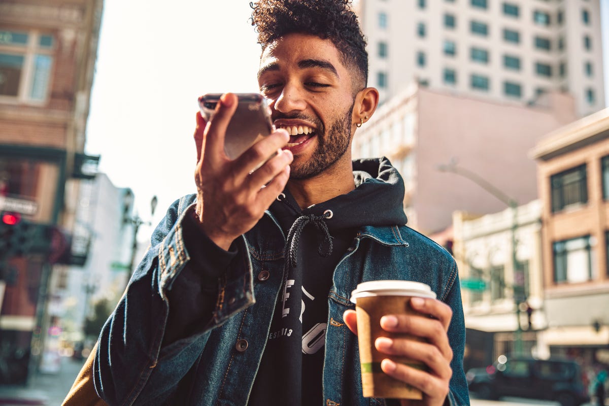 Young man with coffee in one hand and smartphone in the other sending a voice message