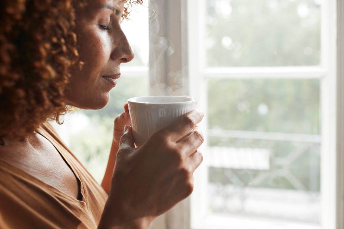 Woman standing by the window and smelling her cup of coffee