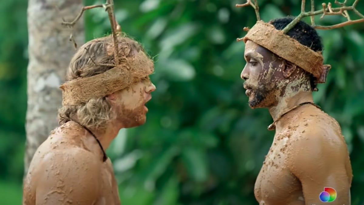 Two reality show contestants covered in mud, wearing fake antlers.
