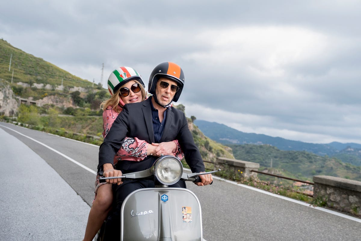 Greg drives a Vespa while Tanya holds on behind him