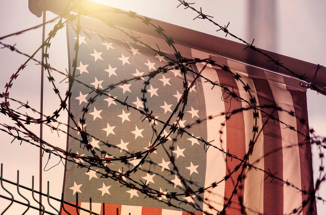 Barbed wire obscures the view of a US flag, pictured at the border.
