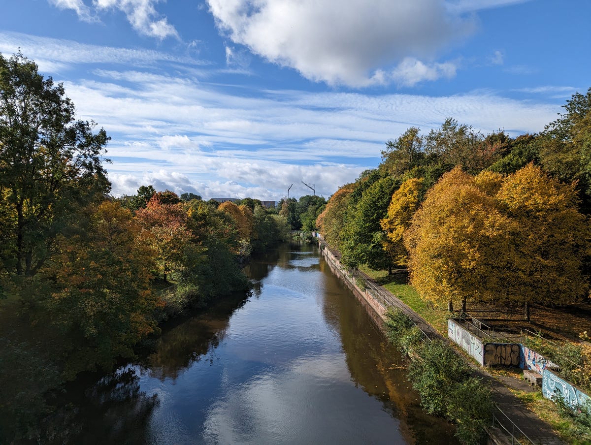 An image showing colorful trees,  river and a blue sky.