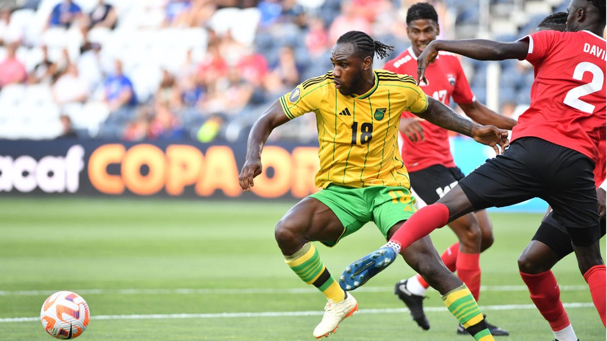 Jamaica soccer player Michail Antonio running to left with the ball while evading two Trinidad & Tobago players