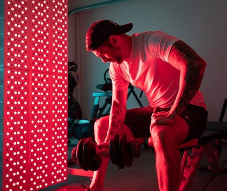 Man does dumbbell bicep curls in front of red light therapy panel