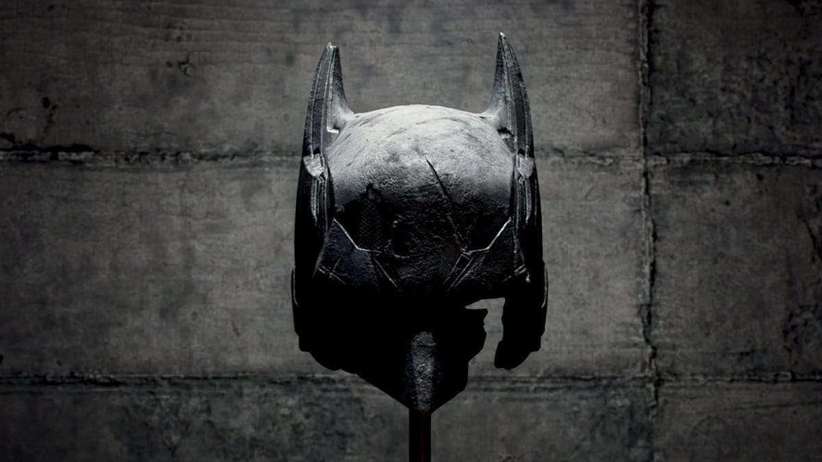 Batman&apos;s broken cowl against a gray wall background in Gotham Knights