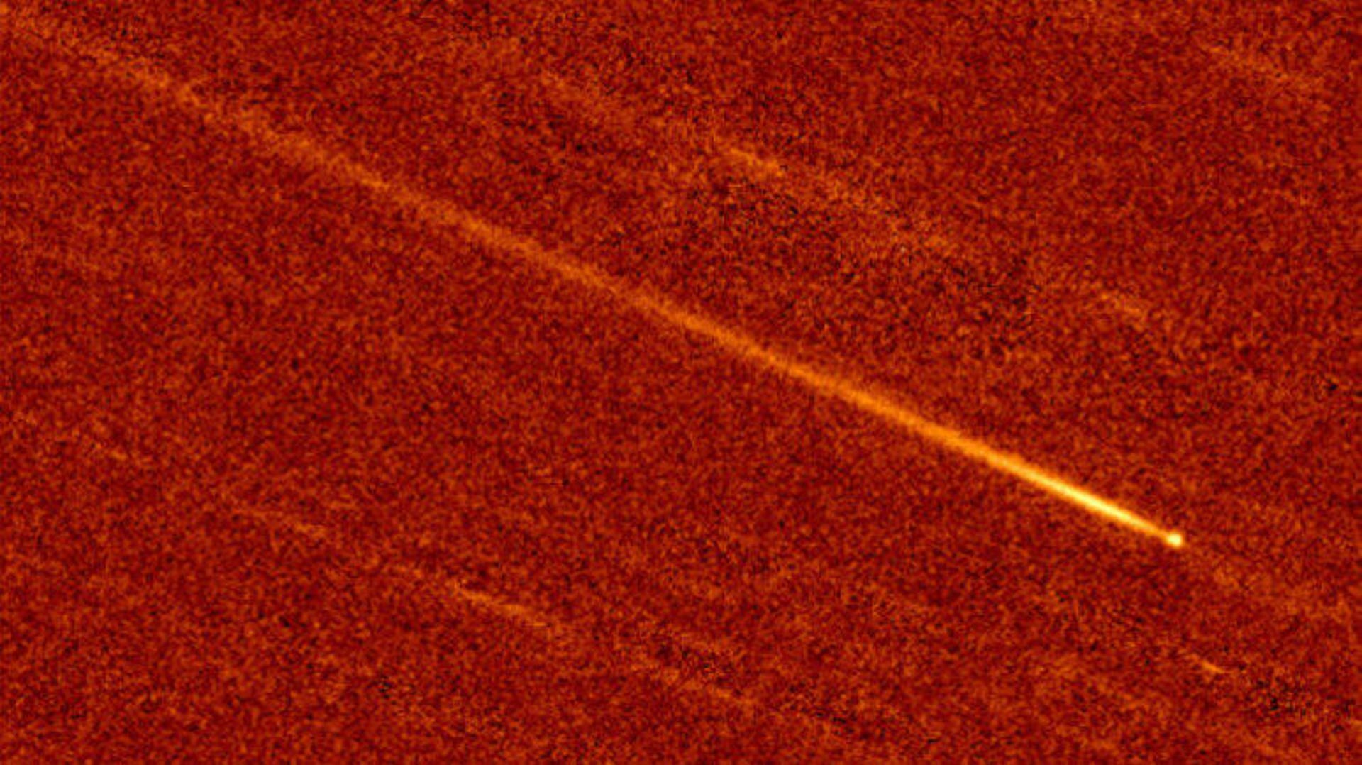 A yellowish streak of light against a red background shows how a near-sun comet developed a tail after close encounter with the sun.