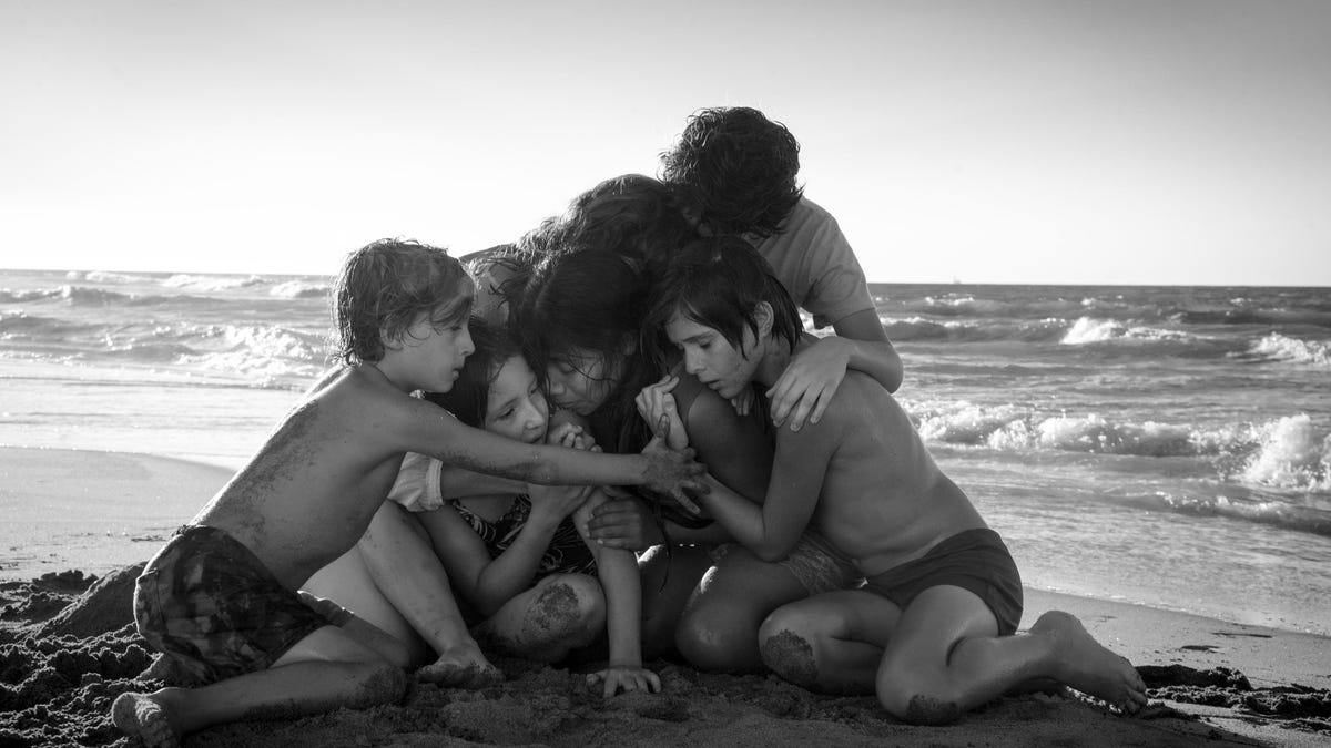 Characters from Roma huddle together on a beach.