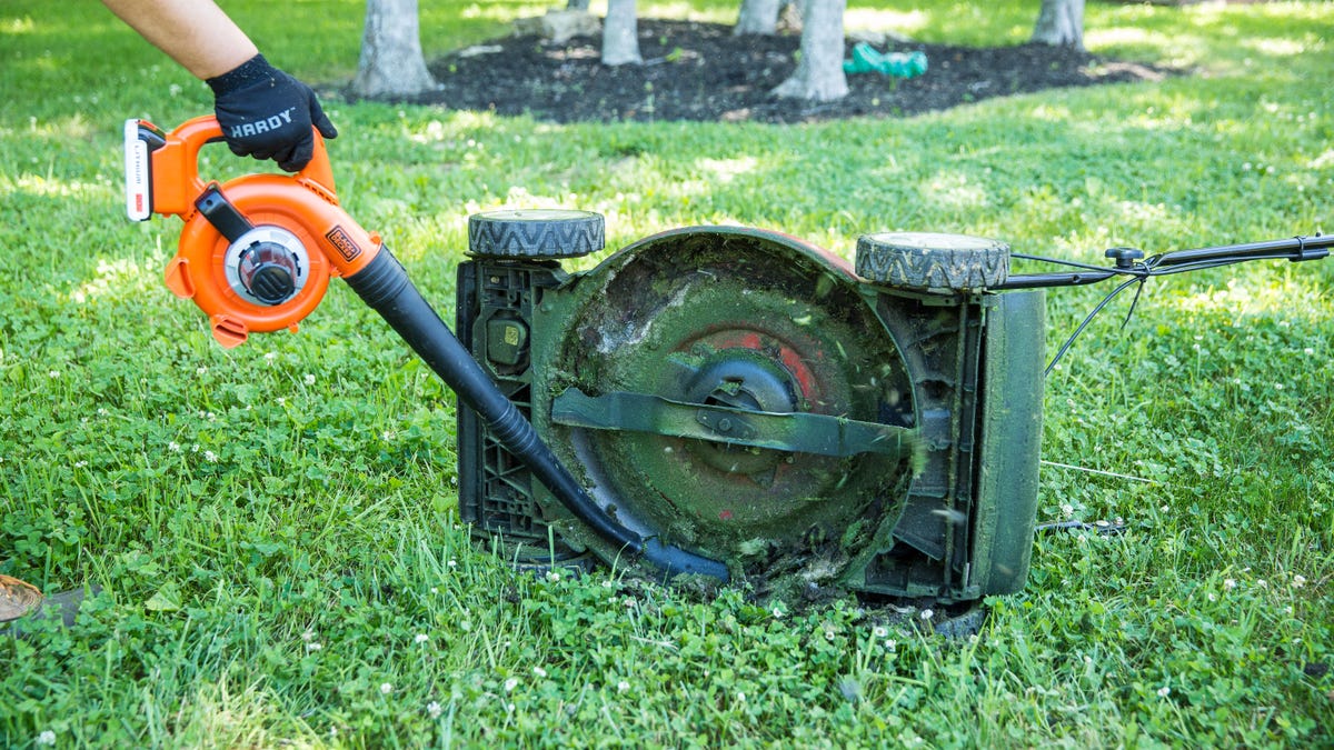 a leaf blower cleans the underside of a lawn mower