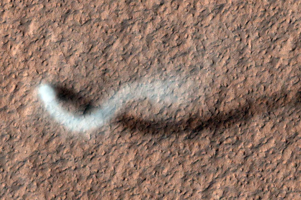 Overhead shot of the reddish Martian landscape, which serves as the backdrop for a sinuous, long white dust devil with a snakelike tail.
