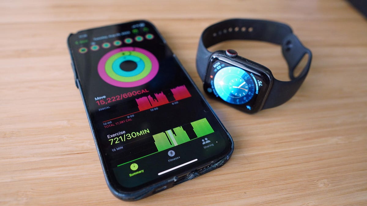 An Apple Watch Series 5 sits on a desk next to an iPhone with the fitness numbers it recorded: a "move" score of 15,222 calories (out of a 690 calorie daily goal) and 721 exercise minutes (out of a 30 minute daily goal).