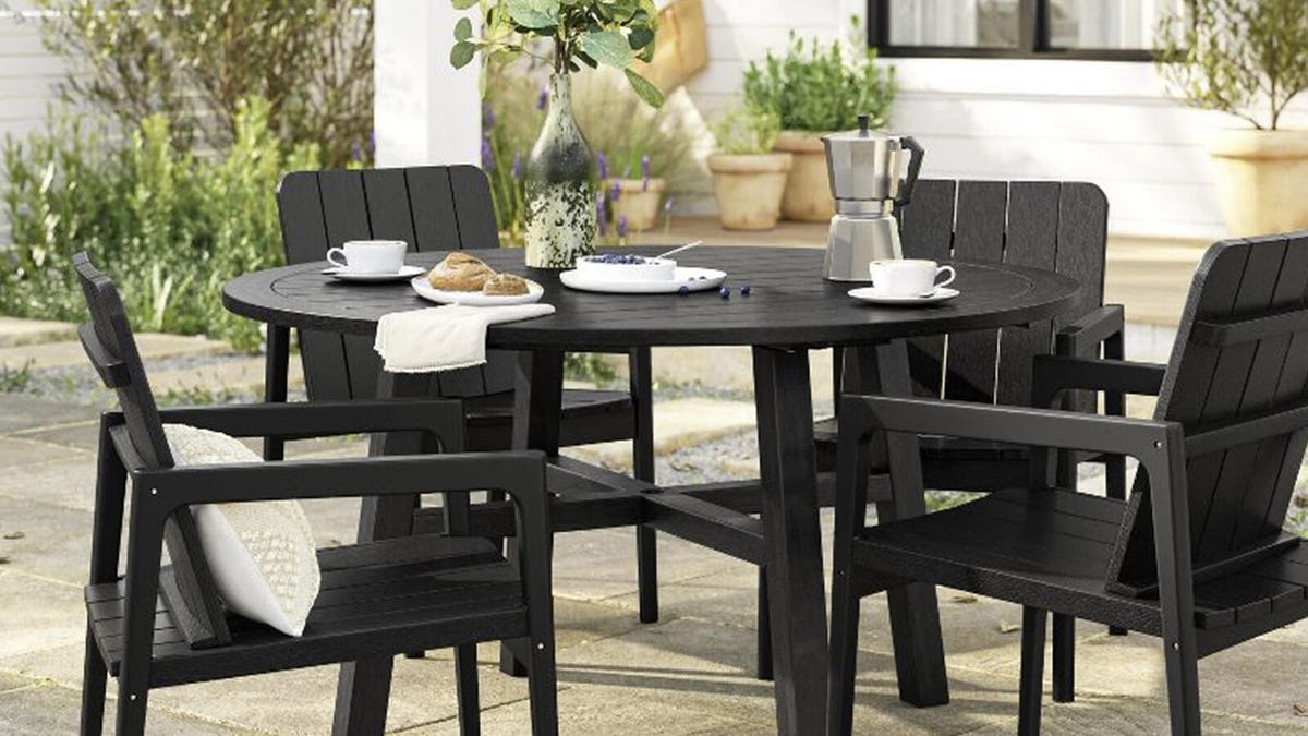 A blackened wood 4-person patio dining set from Smith and Hawken sits on pavers in a yard surrounded by plants.